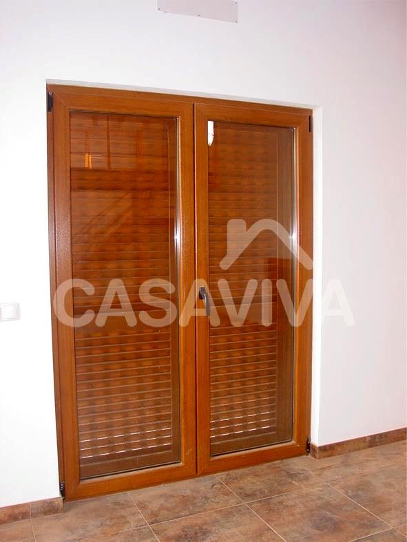Nueva puerta exterior con dos hojas abatibles, en vidrio y enmarcado de madera.Puerta exterior en madera.