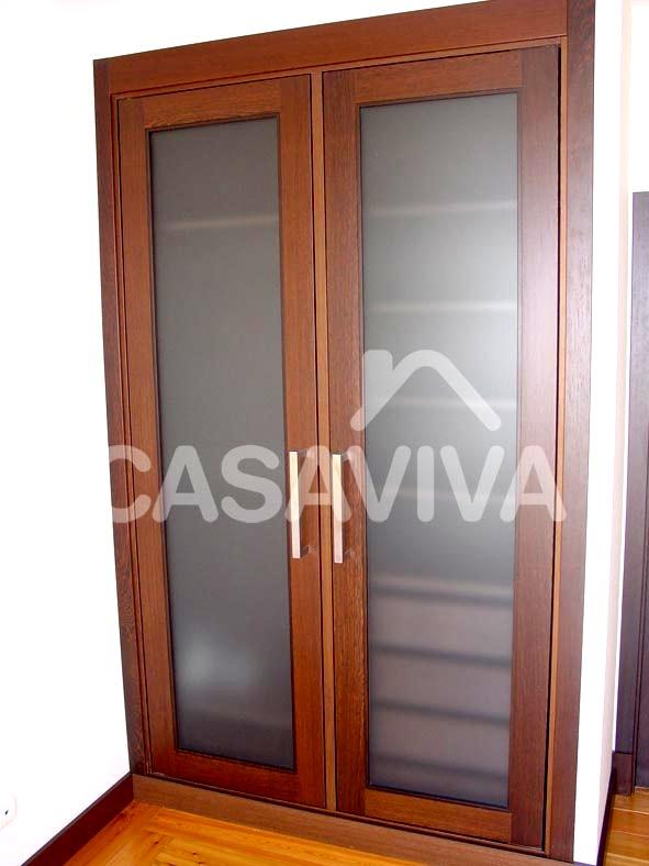 Armario empotrado con puertas abatibles en cristal opaco y bordes en madera.