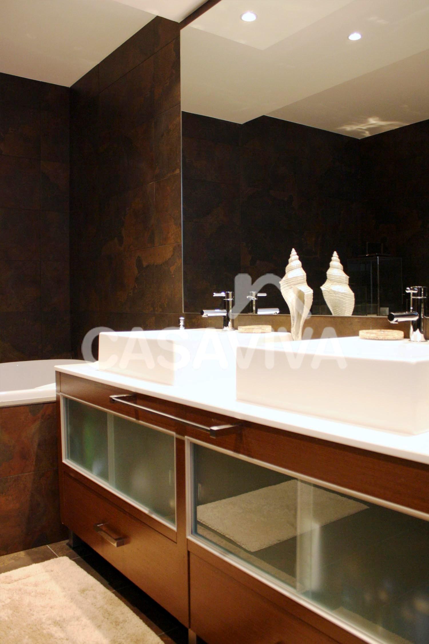 Mueble de bao bajo encimera de piedra, lavabo y grifo mezclador.Revestimiento de paredes en azulejo cermico con terminacin especial.